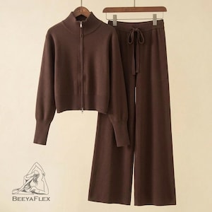 May include: A brown knitwear set featuring a zip-up jacket with a high collar and wide-leg pants with a drawstring waist. The set is displayed on a wooden hanger. The logo "BEEAYAFLEX" is visible in the lower left corner.