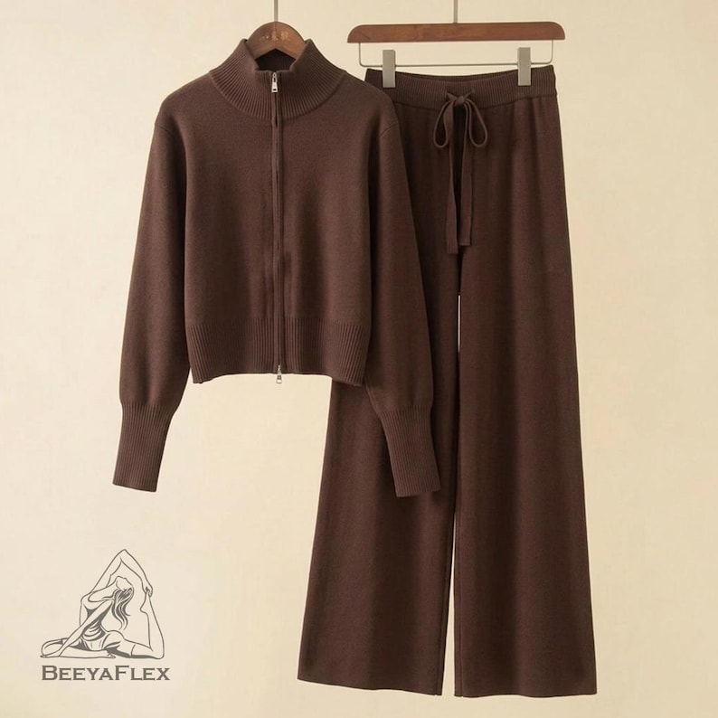 May include: A brown knitwear set featuring a zip-up jacket with a high collar and wide-leg pants with a drawstring waist. The set is displayed on a wooden hanger. The logo "BEEAYAFLEX" is visible in the lower left corner.