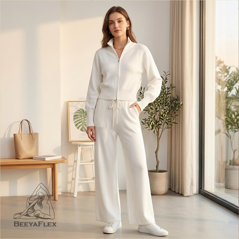 May include: A matching white knitwear set, featuring a zip-up jacket and wide-leg pants. The jacket has a high collar and the pants have a drawstring waist. The outfit is paired with white sneakers. The brand name "BEEAYAFLEX" is visible.