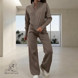 May include: A two-piece knit set in a neutral brown color. The set includes a zip-up jacket with a high collar and wide-leg pants. The outfit is made of a soft, textured material, perfect for casual wear.