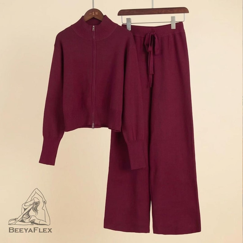 May include: A burgundy knitwear set, including a zip-up sweater with a high collar and wide-leg pants with a drawstring waist. The set is displayed on a hanger against a neutral background. The brand name "BEE YAFLEX" is visible at the bottom.