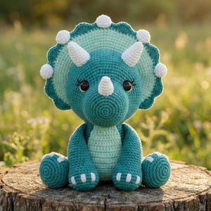 May include: A handmade crochet triceratops dinosaur in shades of teal and mint green, with white horns and accents. The stuffed animal has large, dark eyes and is sitting on a wooden stump. The background is a blurred, natural setting.
