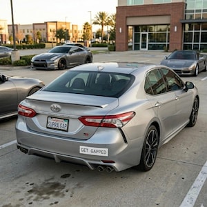 Puede incluir: Toyota Camry plateado con llantas negras y alerón trasero. La matrícula dice "SUPRA GAP" y una pegatina dice "GET GAPPED". Otros coches son visibles en el fondo.