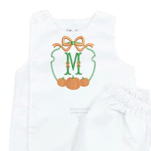 May include: A white sleeveless vest and matching bloomer set featuring an embroidered design on the chest. The embroidery displays a green letter M framed by a green vine, an orange bow at the top, and three orange pumpkins at the bottom.