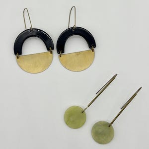 May include: Two pairs of earrings. One pair features a black half-circle above a gold half-circle. The other pair has a light green circular stone with a long, thin, gold-colored post.
