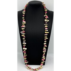 May include: A long necklace featuring irregular, chip-shaped beads in shades of cream, beige, and vibrant pink. The beads are strung together with small, dark brown spacer beads, creating a textured, multi-colored strand that hangs in a loop.