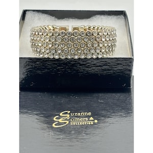 May include: A silver-toned bracelet with multiple rows of clear, round rhinestones. The bracelet is displayed in a black box with the "Suzanne Somers Collection" logo in gold lettering.