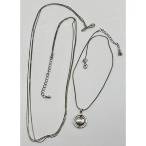 May include: Two silver-toned necklaces. One is a long, multi-strand chain. The other has a pendant with a circular frame and a pearlescent center. Both necklaces have adjustable chain lengths.