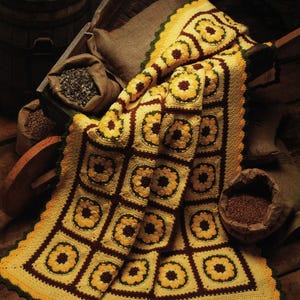 Peut inclure: Une couverture au crochet faite à la main avec un motif de tournesol en jaune, marron et vert. La couverture est drapée sur une brouette en bois, avec des sacs de jute de graines et un tonneau de fleurs en arrière-plan. Dimensions : environ 152 cm x 178 cm.