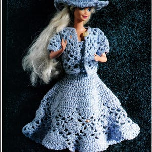 May include: A doll dressed in a light blue crochet ensemble: a hat, jacket, and dress. The dress features a flared skirt with decorative cutouts. The doll has long, blonde hair, set against a dark backdrop.
