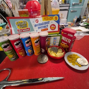 May include: A collection of miniature food items, including Pringles cans, Cheez-It box, and a small bowl of chips, arranged on a red surface. The scene includes a sign that reads "Mini Verse Real Brands" and "Outrageous Specials".