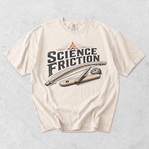 Peut inclure: Un t-shirt couleur crème avec une impression graphique représentant un kit d'allumage de feu par friction, accompagné du texte "SCIENCE FRICTION" en caractères gras foncés et d'une petite icône de flamme orange au sommet du motif.