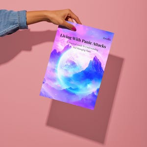 以下が含まれることがあります： 「Living With Panic Attacks」というタイトルの本の表紙を人が持っています。表紙には、紫、青、白の色合いで描かれた山脈と大きな光る球体の鮮やかなイラストが描かれています。この本は、パニック発作を理解し、管理するための実用的なガイドです。