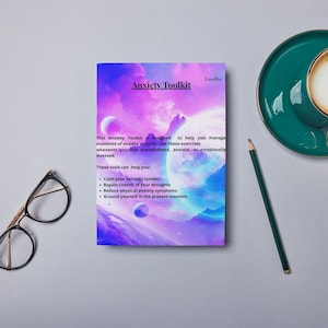 May include: Anxiety Toolkit booklet with a colorful space-themed cover, a teal coffee cup and saucer, a pencil, and eyeglasses. The booklet's text reads: "This Anxiety Toolkit is designed to help you manage moments of anxiety or panic..." and lists tools to help.