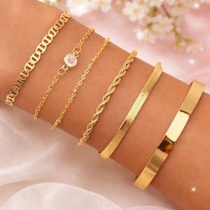 May include: A selection of six gold-coloured bracelets in diverse styles. The bracelets feature a chain link design, a fine chain with a clear stone, a beaded chain, a rope-style bracelet, a herringbone bracelet, and a solid bangle.