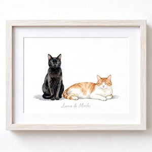 May include: A framed watercolor illustration featuring a black cat sitting upright next to a ginger and white tabby cat lying down. Below the cats, the text "Luna & Mochi" is printed in a simple script font. The artwork is encased in a light wood frame.