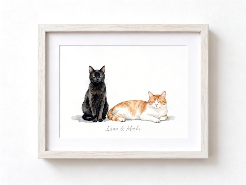 May include: A framed watercolor illustration featuring a black cat sitting upright next to a ginger and white tabby cat lying down. Below the cats, the text "Luna & Mochi" is printed in a simple script font. The artwork is encased in a light wood frame.