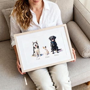 May include: A framed watercolor-style print featuring a black and white husky, a small calico cat, and a black Labrador retriever sitting side-by-side. The names Trek, Osho, and Remy are printed in black script beneath each respective animal illustration.