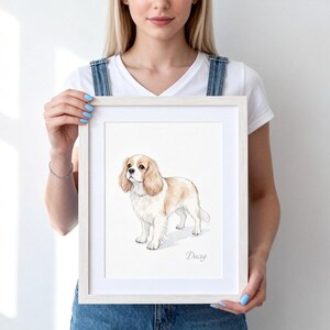 May include: A framed art print featuring a watercolor illustration of a white and tan Cavalier King Charles Spaniel standing in profile. The dog has long, floppy ears and a soft expression. The name Daisy is written in cursive script below the dog.