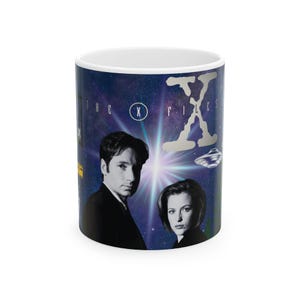 May include: A white ceramic mug featuring a dark blue space-themed background with a bright central light. It displays black and white portraits of two people, a silver flying saucer, and the text THE X FILES with a large stylised letter X.