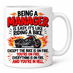 May include: A white ceramic mug featuring a graphic of a black motorcycle surrounded by orange and yellow flames. The text reads: BEING A MANAGER IS EASY, IT'S LIKE RIDING A BIKE. EXCEPT THE BIKE IS ON FIRE. YOU'RE ON FIRE. EVERYTHING IS ON FIRE. AND YOU'RE IN HELL.