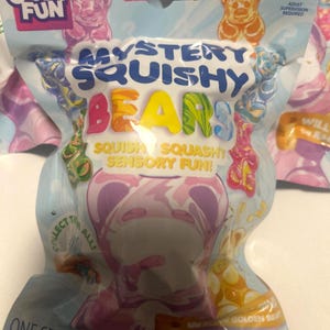 May include: A light blue plastic pouch containing Mystery Squishy Bears, series 5. The packaging features colorful gummy bear graphics, the text "Crazy Fun," "Mystery Squishy Bears," "Squish Squashy Sensory Fun!," "Collect Them All!," and "One Set." It is labeled for ages 3+.