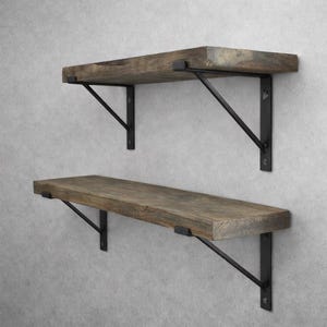 Könnte beinhalten: Zwei rustikale Holzregale mit schwarzen Metallhalterungen sind an einer hellgrauen Wand montiert. Die Regale haben eine natürliche Holzmaserung und sind rechteckig. Die Halterungen sind abgewinkelt.