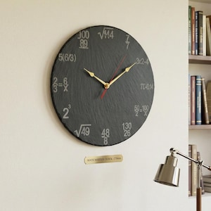 Op de afbeelding: Een ronde, zwarte leien klok met gouden wijzers en een rode secondewijzer. De klok heeft wiskundige vergelijkingen op de wijzerplaat. Een messing plaatje eronder leest "MATH MASTER CLOCK - 270mm".