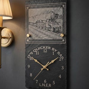 May include: Black slate clock featuring a train illustration and gold hands. The clock face reads "IT'S QUICKER BY RAIL" and "L.N.E.R."