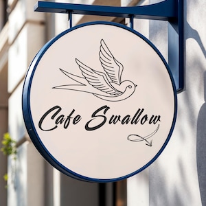 May include: A round cafe sign with a blue frame and mounting hardware. The sign features a cream-colored background with a black line drawing of a swallow and the words "Cafe Swallow" in a script font.