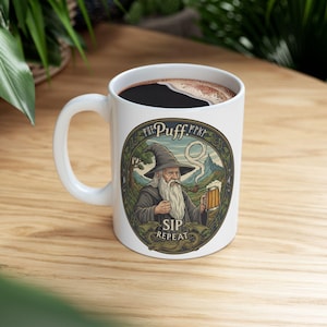 May include: White ceramic mug with a whimsical illustration of a wizard smoking a pipe and holding a mug of beer. The mug has the words "Puff...Sip Repeat" around the image. The mug is filled with dark liquid.