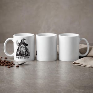 May include: White ceramic mug with a black and white illustration of a wizard smoking a pipe and holding a beer stein. The text "Puff. Sip. Repeat." is below the image. Two additional blank mugs are also visible.