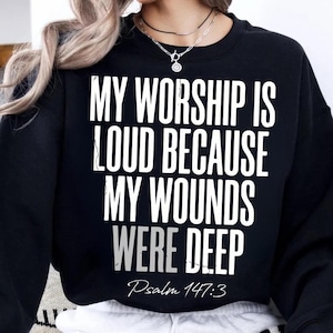 Pode incluir: Camisola preta com o texto branco "MY WORSHIP IS LOUD BECAUSE MY WOUNDS WERE DEEP". A referência bíblica "Psalm 147:3" está escrita abaixo em uma fonte de script.