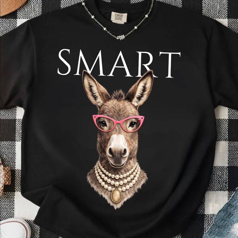 May include: Black t-shirt with the word "SMART" in white block letters. The shirt features a graphic of a donkey wearing pink glasses and a pearl necklace. The donkey is brown with a white muzzle.