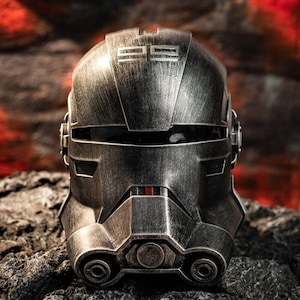 May include: A metallic silver helmet with the number "99" on top. The helmet has a weathered appearance and is set against a dark, textured background. The helmet has a red accent.
