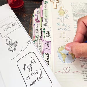 May include: A Bible with colourful book tabs and a white insert featuring the text How Great Thou Art and Light of the World alongside a lantern illustration. The open page shows a hand-coloured globe, a heart, and the text Light of the world.
