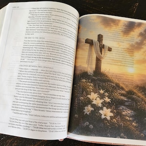 Peut inclure: Un livre ouvert montrant deux pages. La page de gauche contient du texte imprim&eacute; de la Bible, sp&eacute;cifiquement Luc 23. La page de droite pr&eacute;sente une illustration en couleur d'une croix en bois drap&eacute;e d'un tissu blanc sur une colline avec des lys blancs.