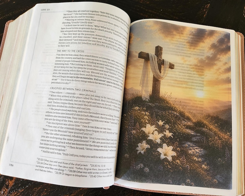 Peut inclure: Un livre ouvert montrant deux pages. La page de gauche contient du texte imprim&eacute; de la Bible, sp&eacute;cifiquement Luc 23. La page de droite pr&eacute;sente une illustration en couleur d'une croix en bois drap&eacute;e d'un tissu blanc sur une colline avec des lys blancs.