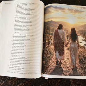 Puede incluir: Biblia abierta con una imagen a página completa de dos personas caminando de la mano hacia una puesta de sol. La imagen está en la página derecha, mientras que la página izquierda muestra el texto de Isaías 41.