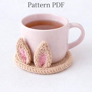 May include: A white ceramic mug with a black handle and the text "But First, Coffee" in a bold, black font. The mug is set against a blurred background, suggesting a cozy setting.