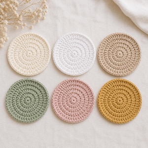 K&ouml;nnte beinhalten: Ein Set aus sechs runden H&auml;keluntersetzern, die in zwei Reihen angeordnet sind. Die Untersetzer weisen ein spiralf&ouml;rmiges Stichmuster auf und sind in verschiedenen Unifarben erh&auml;ltlich, darunter Creme, Wei&szlig;, Beige, Salbeigr&uuml;n, Altrosa und Senfgelb.