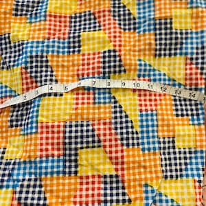 May include: A colorful fabric with a checkered pattern in blue, yellow, red, and orange. The fabric is made of a soft, lightweight material and has a relaxed, casual feel.