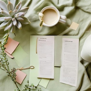 Può includere: Una natura morta con una tazza bianca e un cucchiaino dorato, una pianta succulenta e un blocco note con testo. La scena è ambientata su tessuto verde, con post-it rosa e una chiave dorata.