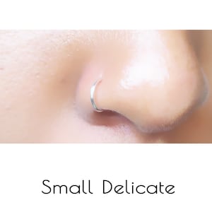 May include: A close-up of a person's nose with a small, silver nose ring. The ring is a simple hoop.