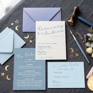 Op de afbeelding: Bruiloft briefpapier set in blauw en wit, inclusief uitnodigingen, detailkaarten en RSVP-kaarten. De afbeelding toont ook een blauwe envelop, gouden ster- en maanversieringen, een lakzegel, een pen en bloemen. De uitnodiging luidt "Rosemary & Andrew".
