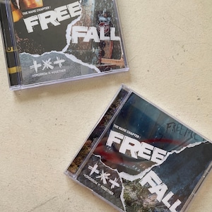 Puede incluir: Dos cajas de CD transparentes. La portada del álbum presenta las palabras "FREE FALL" en blanco, con un efecto de papel rasgado sobre un fondo oscuro. También se ve el texto "THE NAME CHAPTER" y "+*+ TOMORROW X + TOGETHER".