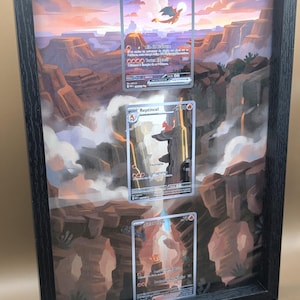 Peut inclure: Cadre noir contenant trois cartes Pokémon, présentées sur un fond de paysage désertique. Les cartes mettent en valeur les personnages et leurs détails. L'arrière-plan représente des canyons et un coucher de soleil.