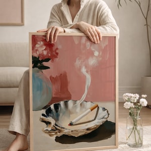 May include: A framed art print featuring a still life composition. The artwork depicts a lit cigarette in a seashell ashtray, with smoke rising against a pink backdrop. A blue vase with flowers is also visible. The frame is made of light-colored wood.