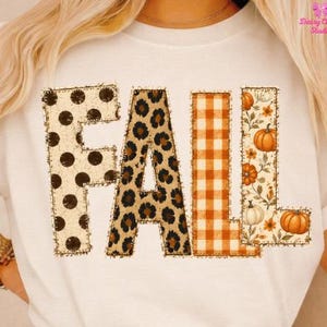 May include: A white short-sleeved t-shirt featuring the word FALL in large block letters. The F has black polka dots, the A has a brown leopard print, the L has an orange and white gingham pattern, and the second L features pumpkins and vines.