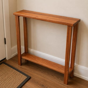 May include: A narrow, wooden console table with a warm, reddish-brown finish. The table has a rectangular top and a lower shelf, supported by four vertical legs. The table is approximately 76 cm long, 25 cm wide, and 76 cm tall.
